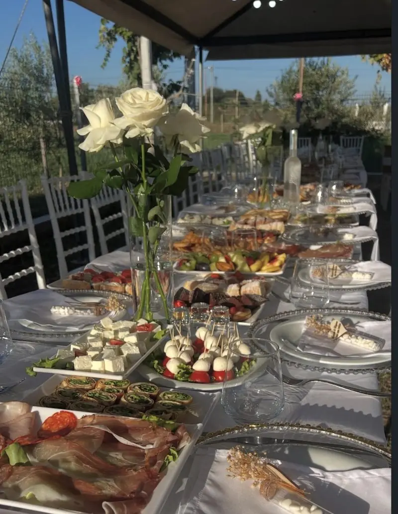 Tavolinë e shtruar në kopsht me trëndafila të bardhë dhe antipasta